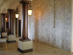 two lamps on pedestals in the middle of a room with stone walls and pillars