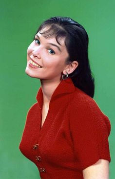 a woman in a red shirt is smiling at the camera while standing against a green background