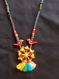 a colorful necklace with beads and tassels on a black cloth covered tablecloth