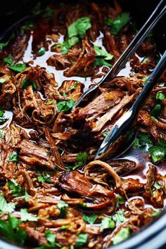 shredded meat and greens in a pot with tongs