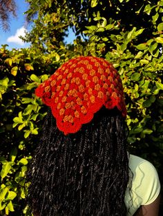 a woman with long black hair wearing a red flowered hat in front of trees