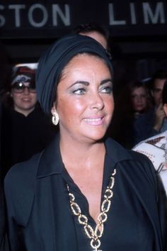 a woman wearing a black shirt and gold necklace in front of a group of people