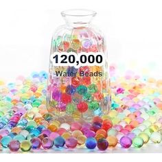 a jar filled with lots of different colored beads on top of a table next to a white background