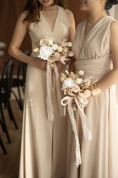 two bridesmaids in beige dresses holding bouquets and smiling at eachother