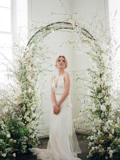 a woman standing in front of an arch with flowers and greenery on the side