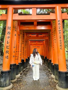 a woman in white is standing under an orange torimi gate with writing on it