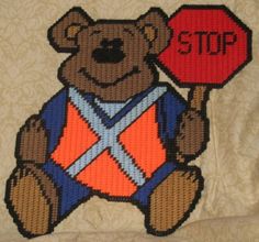 a cross stitch teddy bear holding a stop sign