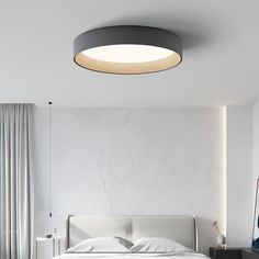 a white bed sitting under a round light fixture in a bedroom next to a window