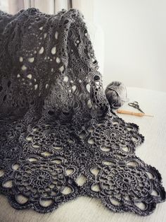 a black crochet doily on a white table cloth with yarn in the background