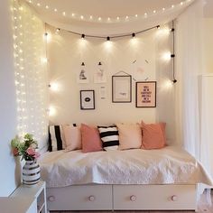 a bedroom with white walls and string lights on the wall above the bed is decorated with pink, black and white pillows