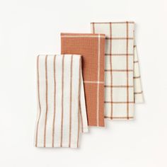 three towels are lined up on a white surface, one is orange and the other is brown