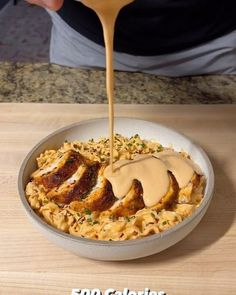 a person pouring sauce on some food in a bowl with macaroni and cheese