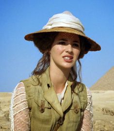 a woman wearing a hat and vest in front of the pyramids at giza