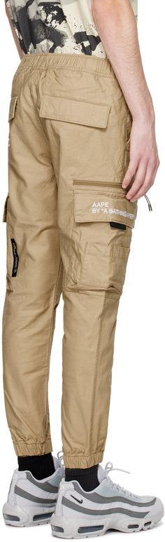 Stretch cotton canvas cargo pants. · Concealed drawstring at elasticized waistband · Four-pocket styling · Zip-fly · Detachable velcro logo patch at front · Logo embroidered at front and back · Flap pocket and zip pocket at outseams · Elasticized cuffs Supplier color: Beige Beige Cotton Parachute Pants For Outdoor, Beige Parachute Pants With Hip Pockets For Streetwear, Cotton Parachute Pants With Flap Pockets For Streetwear, Beige Cargo Style Parachute Pants For Streetwear, Urban Beige Cargo Pants With Cargo Pockets, Beige Cargo Pants With Hip Pockets For Streetwear, Beige Cargo Pants With Patch Pockets For Outdoor, Techwear Parachute Pants With Flap Pockets For Streetwear, Beige Parachute Pants With Patch Pockets For Streetwear