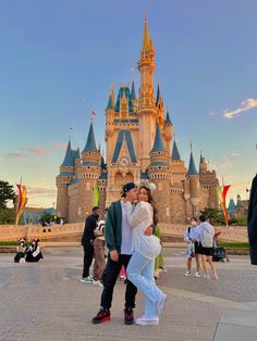 a man and woman kissing in front of a castle at disney world during the day