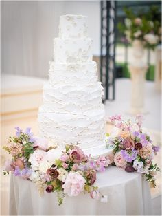 a wedding cake sitting on top of a table covered in flowers and greenery next to a vase