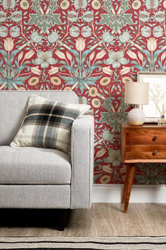 a chair sitting in front of a red wallpaper with flowers and leaves on it