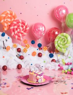 a pink table topped with a cake covered in frosting and lollipops