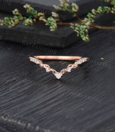 a rose gold ring with three diamonds on it and some greenery in the background