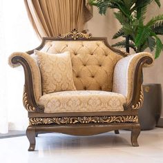 an ornately decorated chair in front of a window with curtains and potted plant