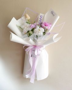 a bouquet of flowers is wrapped in white paper and tied with a pink ribbon on the wall