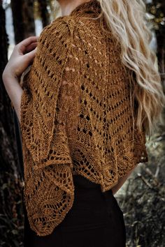 a woman with long blonde hair wearing a brown knitted shawl in the woods