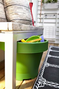 a green trash can sitting on top of a wooden floor next to a white couch