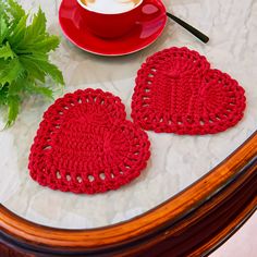 two crocheted heart coasters on a table next to a cup of coffee