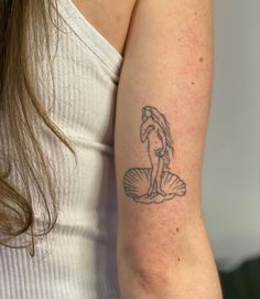 a woman's arm with a tattoo on it that has a mermaid sitting on a shell