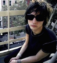 a man with sunglasses sitting on top of a balcony next to a building and looking at the camera