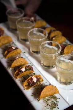 a long white tray topped with lots of food next to glasses filled with water and sauces