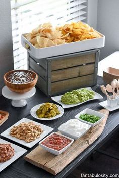 a table topped with plates of food and bowls of dips next to a box of chips