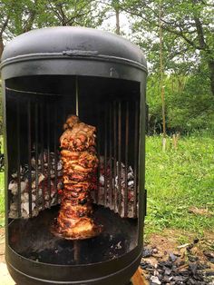 there is a large grill with meat on it in the grass and trees behind it