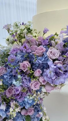 a wedding cake with purple and blue flowers on it's side, in front of a white background