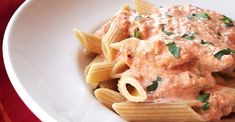 a white bowl filled with pasta covered in sauce and garnished with parsley