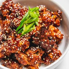 a white bowl filled with meat covered in sesame seeds and garnished with green onions