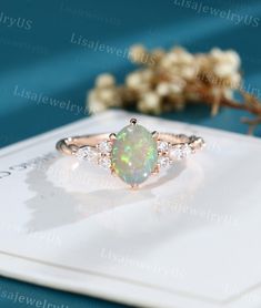 an opal and diamond ring sits on top of a card next to some flowers