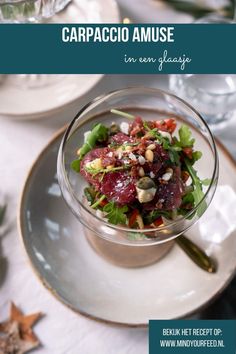 a salad in a glass bowl on top of a white plate with green leaves and nuts