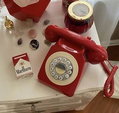 an old fashioned red phone sitting on top of a table next to other items and glassware