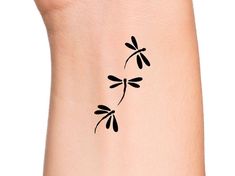 a small black tattoo on the side of a woman's arm, with two dragonflies