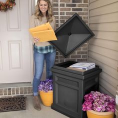 a woman standing in front of a door with a box and some flowers next to her