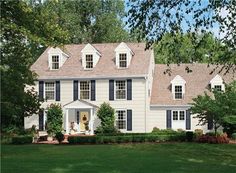 a yellow house with green shutters on the front and side windows, surrounded by trees