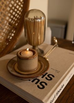 a book with a candle on it sitting on a table next to a wicker chair