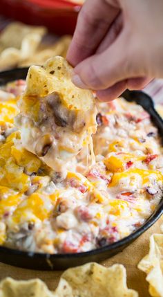 a hand dipping a tortilla chip into a skillet filled with cheesy dip