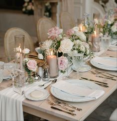 the table is set with white and pink flowers, silverware, candles and napkins