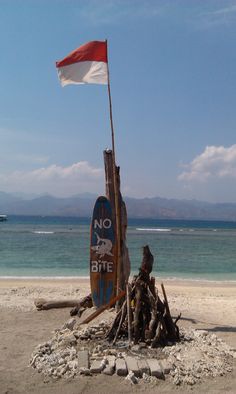 a boat sitting on top of a sandy beach next to the ocean with a flag