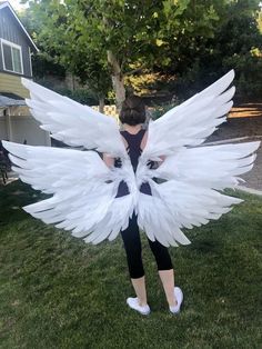 a woman in black shirt and white wings standing on grass