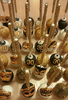 a table topped with lots of cake pops covered in gold and black decorations