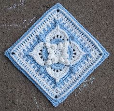 a crocheted square with a flower in the middle is laying on the ground