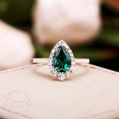 an engagement ring with a pear shaped green stone surrounded by small white diamond halos